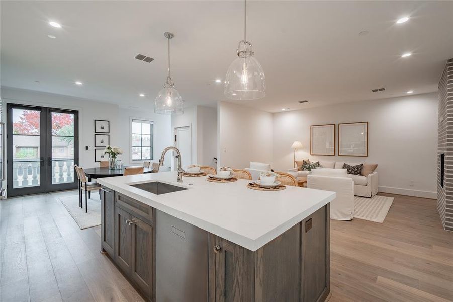 Kitchen featuring sink, an island with sink, decorative light fixtures, french doors, and light wood-type flooring