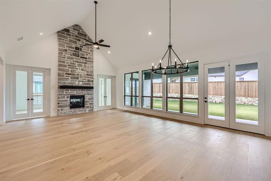 Unfurnished living room featuring ceiling fan with notable chandelier, french doors, a stone fireplace, light hardwood / wood-style floors, and high vaulted ceiling