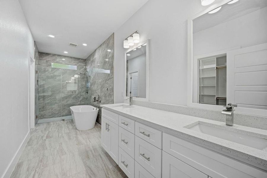 Spacious bathroom featuring a dual vanity with white cabinetry and light-toned countertops, a freestanding soaking tub, a glass-enclosed shower with tiled walls, and wood-finish flooring Spacious bathroom featuring a dual vanity with white cabinetry and light-toned countertops, a freestanding soaking tub, a glass-enclosed shower with tiled walls, and wood-finish flooring