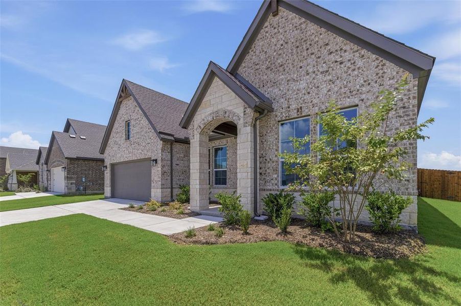 Brick and stone exterior featuring an arched entry, dark trim accents, a concrete driveway, and a manicured lawn Brick and stone exterior featuring an arched entry, dark trim accents, a concrete driveway, and a manicured lawn