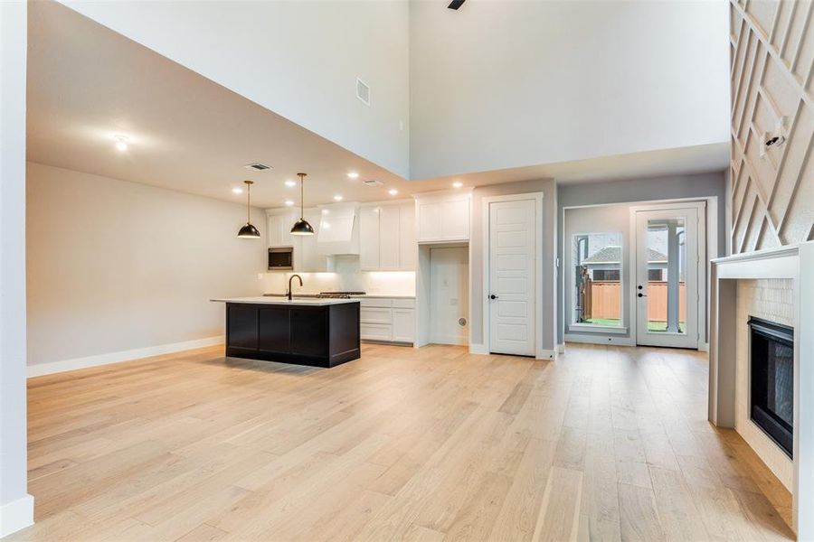 Kitchen featuring light hardwood / wood-style floors, pendant lighting, white cabinets, and a kitchen island with sink