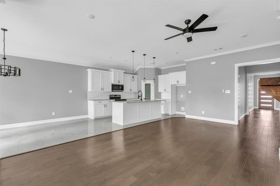 Unfurnished living room featuring ornamental molding, dark wood-type flooring, sink, and ceiling fan with notable chandelier