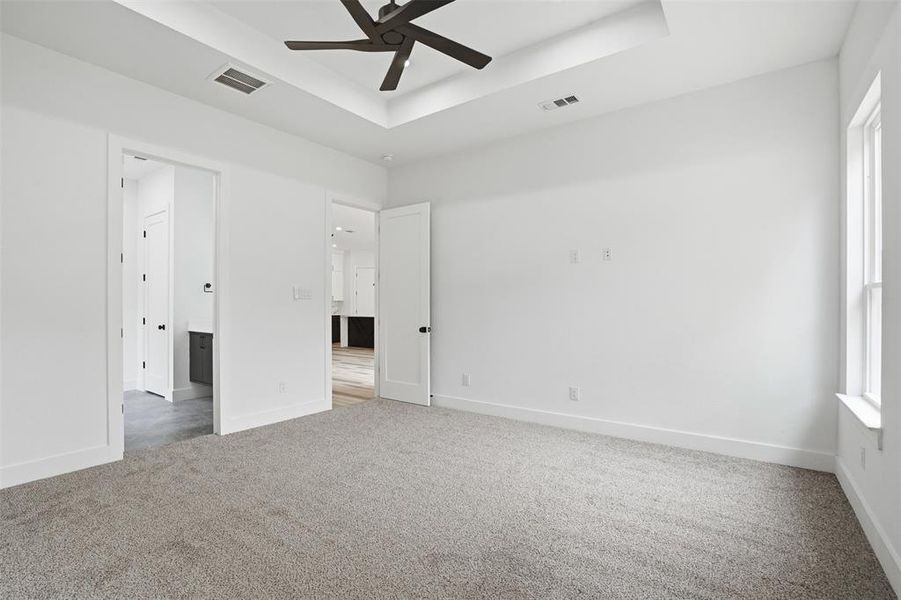 Spacious room with gray carpeting, a tray ceiling featuring a dark-toned ceiling fan, and white walls