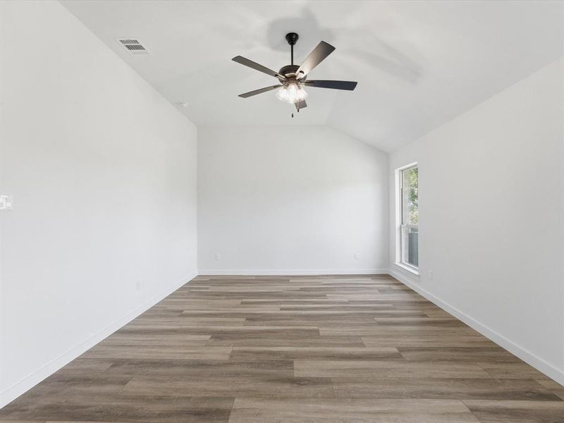 Spacious room featuring vaulted ceilings, wood-finish flooring, a contemporary ceiling fan, and a large window Spacious room featuring vaulted ceilings, wood-finish flooring, a contemporary ceiling fan, and a large window