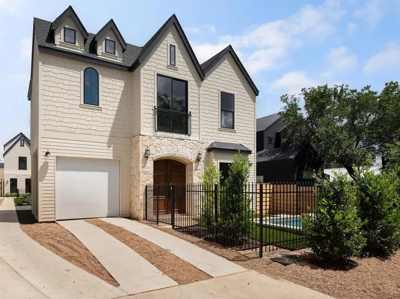 A charming two-story residence with a stone facade and dormer windows, featuring a private fenced yard and driveway.