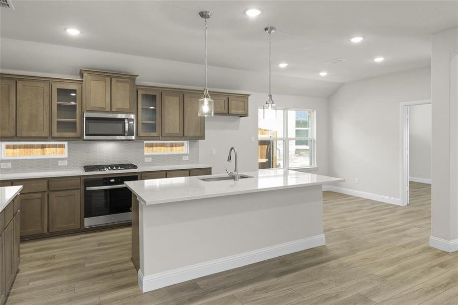 Kitchen featuring decorative light fixtures, backsplash, a kitchen island with sink, appliances with stainless steel finishes, and sink