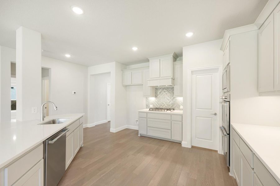 White kitchen with herringbone tile backsplash, quartz countertops, and light hardwood floors
