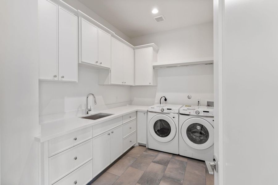 A spacious laundry room features extensive cabinetry, a utility sink, and dedicated space for full-size appliances, combining practicality with polished design.
