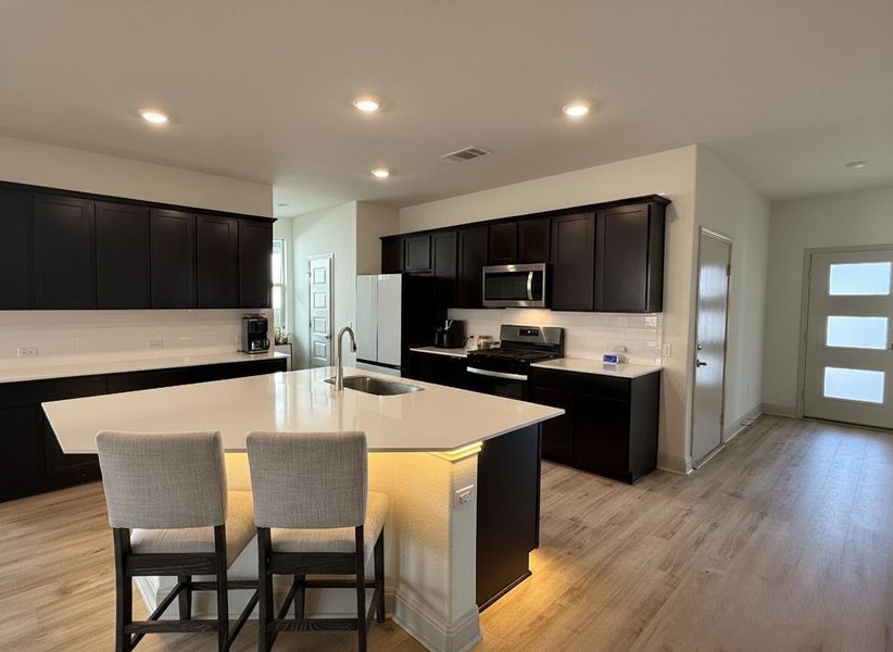 Kitchen featuring dark cabinetry, stainless steel appliances, light wood-style flooring, recessed lighting, and decorative backsplash
