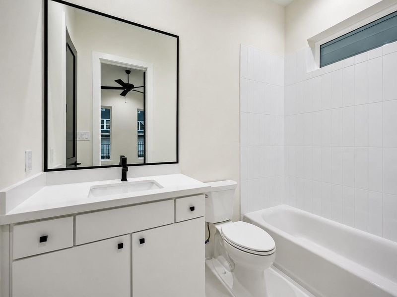 The adjoining full bathroom continues the home’s modern black-and-white aesthetic with a streamlined white vanity, black-framed mirror, matte black faucet, and clean white finishes. The tub and shower combination is surrounded by bright tile, while a horizontal window brings in natural light. Ample vanity storage and crisp contemporary details create a polished, functional space. The adjoining full bathroom continues the home’s modern black-and-white aesthetic with a streamlined white vanity, black-framed mirror, matte black faucet, and clean white finishes. The tub and shower combination is surrounded by bright tile, while a horizontal window brings in natural light. Ample vanity storage and crisp contemporary details create a polished, functional space.