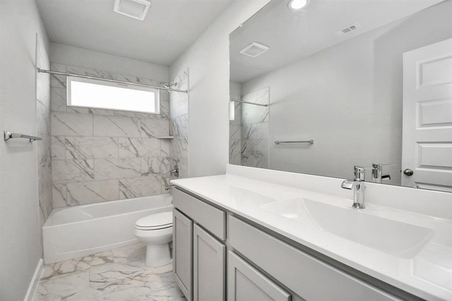 Secondary bath features tile flooring, bath/shower combo with tile surround, light stained wood cabinets, beautiful light countertop.