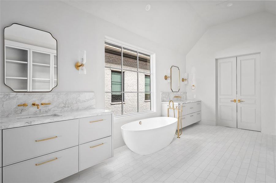 Exuding timeless elegance, the custom-designed primary bathroom features Dover White marble dual vanities lit by Aerin sconces. A freestanding Victoria + Albert tub with Waterworks tub filler sits beneath a large window, enhancing the airy ambiance.