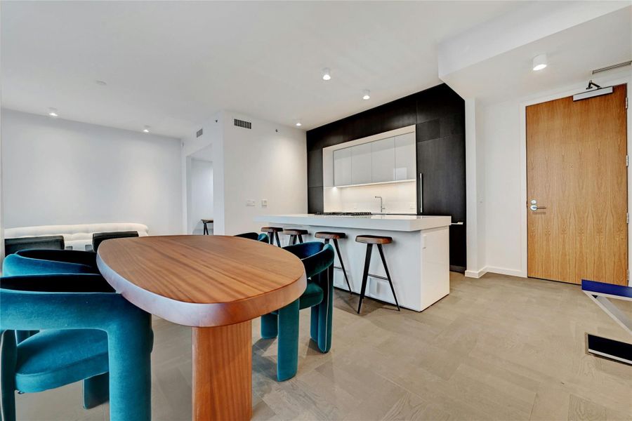 A modern, open-concept kitchen, dining and living area. The kitchen features a sleek, minimalist design with a large island at its center, topped with white-colored stone countertop. The island includes a built-in gas cooktop and stainless steel oven. Furnishings provided by Scott + Cooner available for purchase separately. A modern, open-concept kitchen, dining and living area. The kitchen features a sleek, minimalist design with a large island at its center, topped with white-colored stone countertop. The island includes a built-in gas cooktop and stainless steel oven. Furnishings provided by Scott + Cooner available for purchase separately.