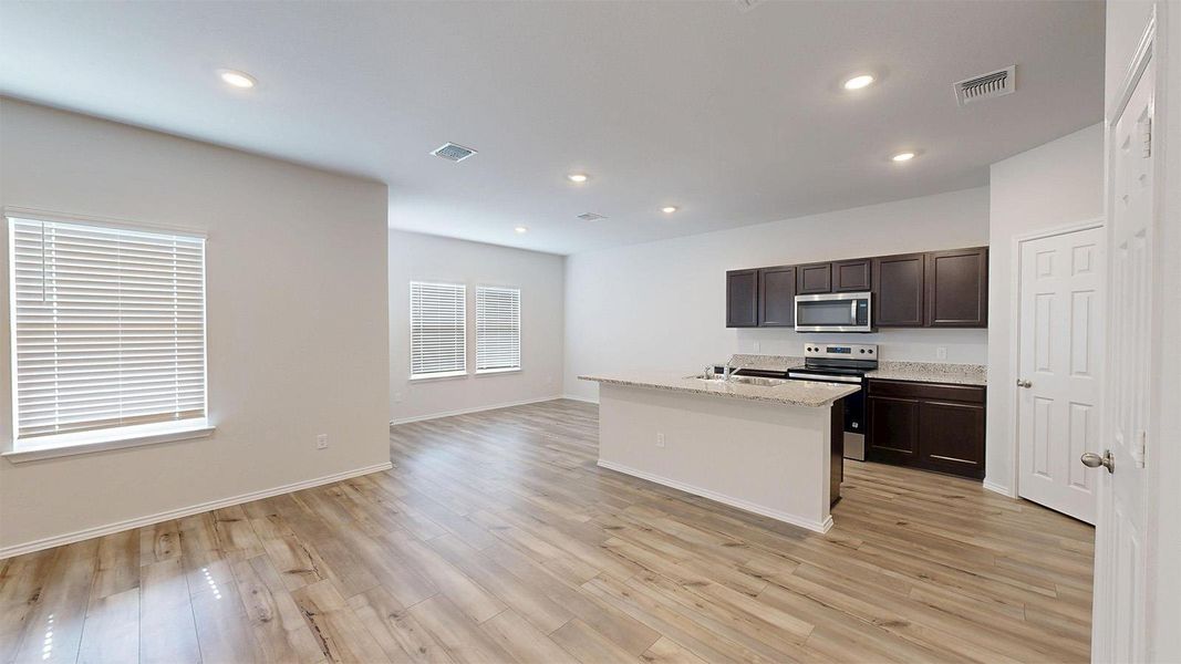 Kitchen with dark wood finish cabinets, stainless steel appliances, a center island with sink, recessed lighting, and light wood-style floors
