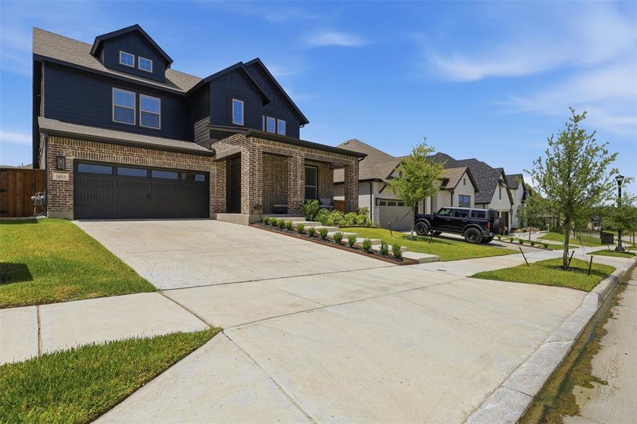 Two-story residence featuring a dark blue siding and brick facade, a two-car garage with a dark door, and a covered front entry Two-story residence featuring a dark blue siding and brick facade, a two-car garage with a dark door, and a covered front entry