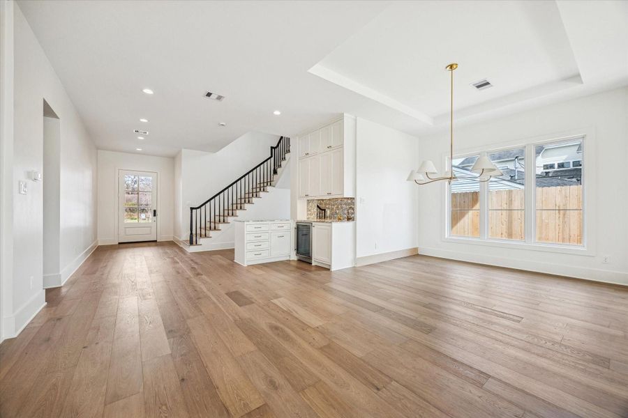 Dining room highlighted by tray ceiling detail and designer chandelier, positioned to capture natural light from oversized windows while flowing seamlessly into the kitchen and living areas for effortless entertaining.