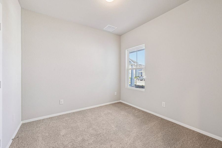 Image of a secondary bedroom with beige walls, tan carpeting and a window