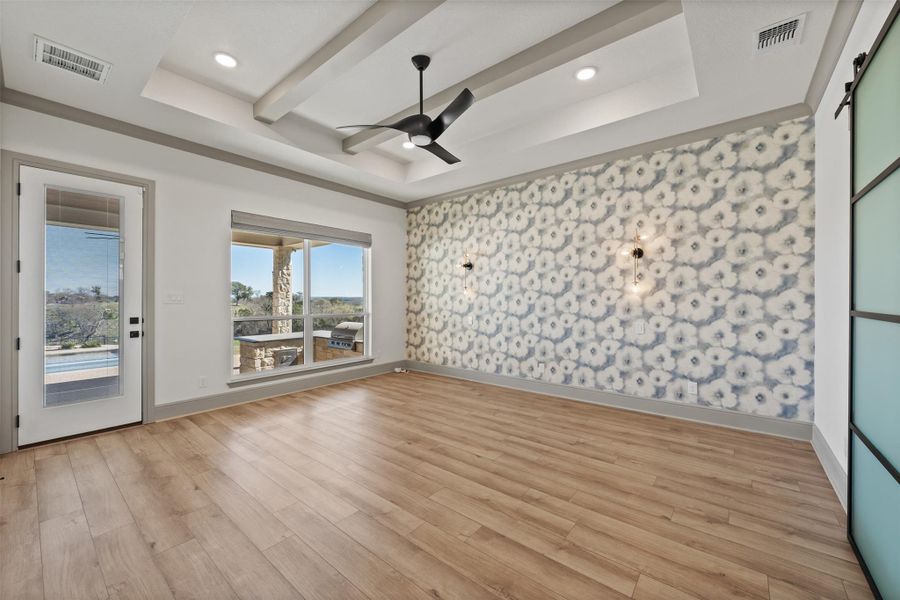 Empty room with light wood finished floors, visible vents, a raised ceiling, and a ceiling fan