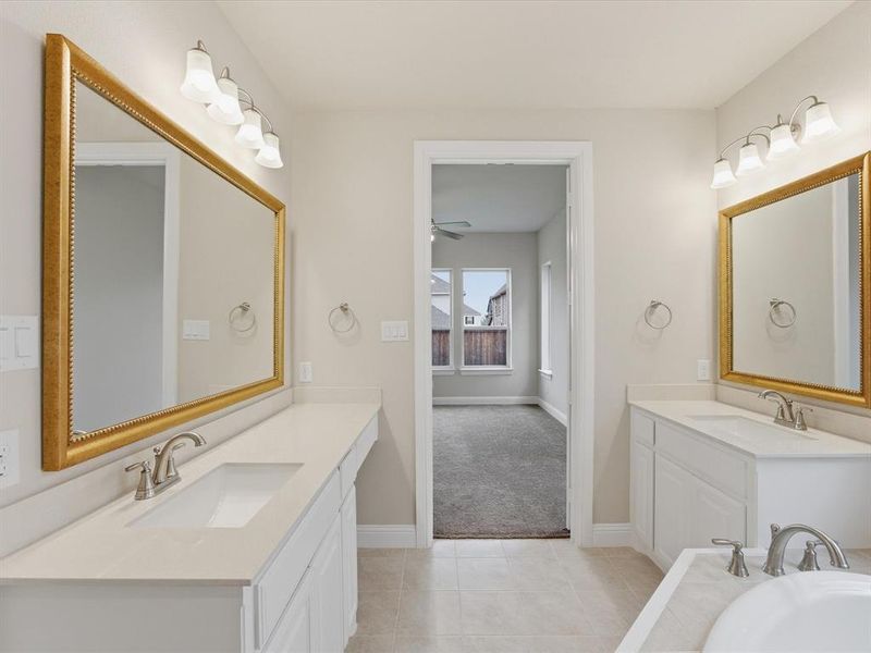 Bathroom featuring a dual vanity with white cabinetry, light-toned countertops, and gold-framed mirrors