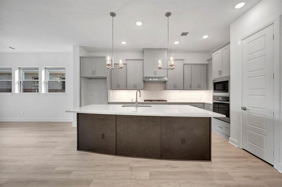 Kitchen with gray cabinets, light wood finished floors, and a center island with sink Kitchen with gray cabinets, light wood finished floors, and a center island with sink
