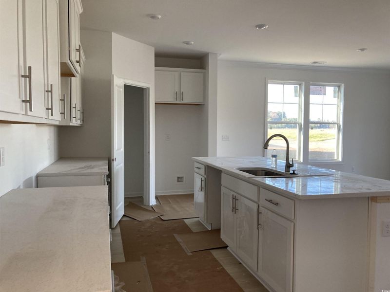 Kitchen with light stone countertops, white cabinetry, a center island with sink, and recessed lighting