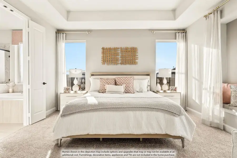 Master bedroom with tray ceiling, carpet flooring, two windows, and ensuite bathroom access through open door.