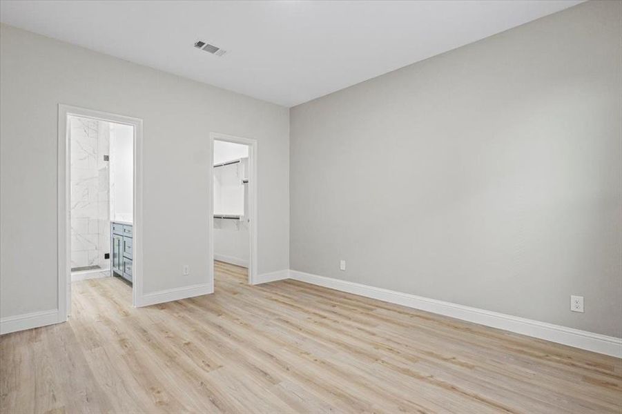 Unfurnished bedroom featuring a walk in closet, ensuite bathroom, and light hardwood / wood-style flooring