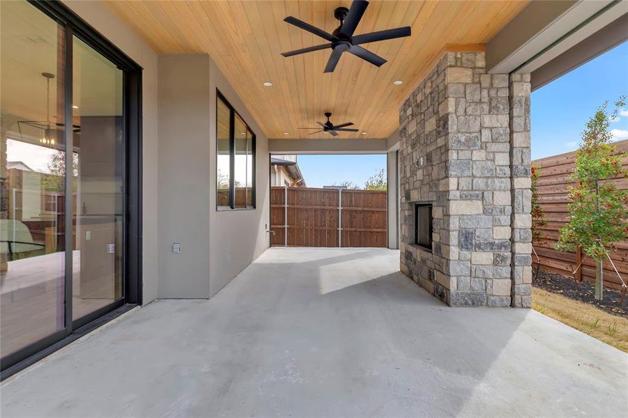 Fenced backyard featuring a ceiling fan, a patio, and an outdoor stone fireplace Fenced backyard featuring a ceiling fan, a patio, and an outdoor stone fireplace