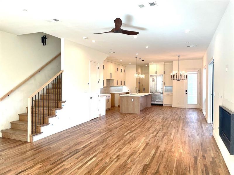 Kitchen with light hardwood floors, white cabinetry, ceiling fan with notable chandelier, an island with sink, and pendant lighting