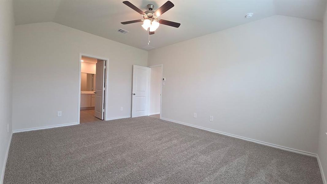 Spacious room featuring vaulted ceilings, light neutral wall paint, and gray carpet flooring