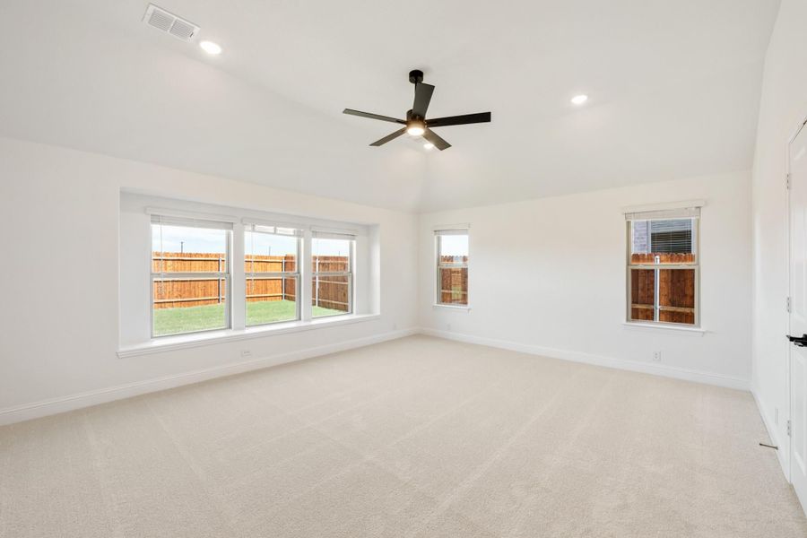 Spacious empty bedroom with carpet, ceiling fan, and multiple windows overlooking a fenced backyard