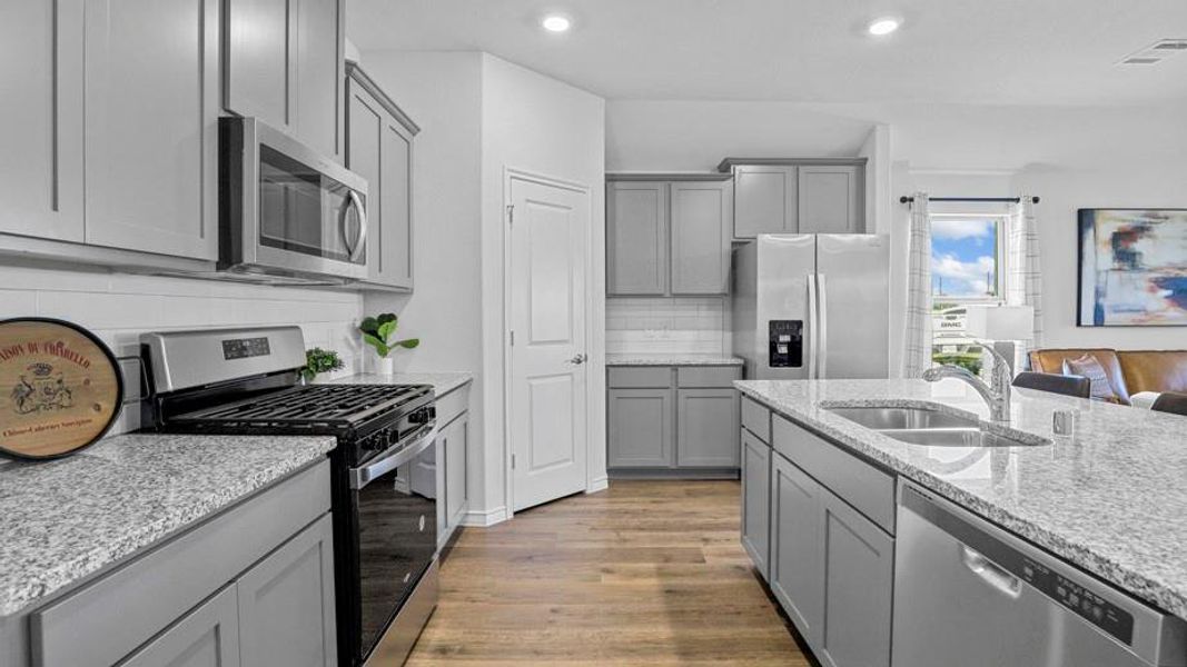 Kitchen featuring appliances with stainless steel finishes, light stone counters, light wood-style floors, gray cabinetry, and decorative backsplash