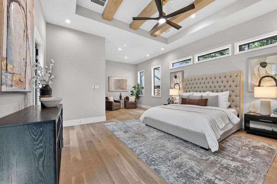 Expansive room featuring light wood-finish flooring, a tray ceiling with exposed wood beams, and a modern ceiling fan Expansive room featuring light wood-finish flooring, a tray ceiling with exposed wood beams, and a modern ceiling fan