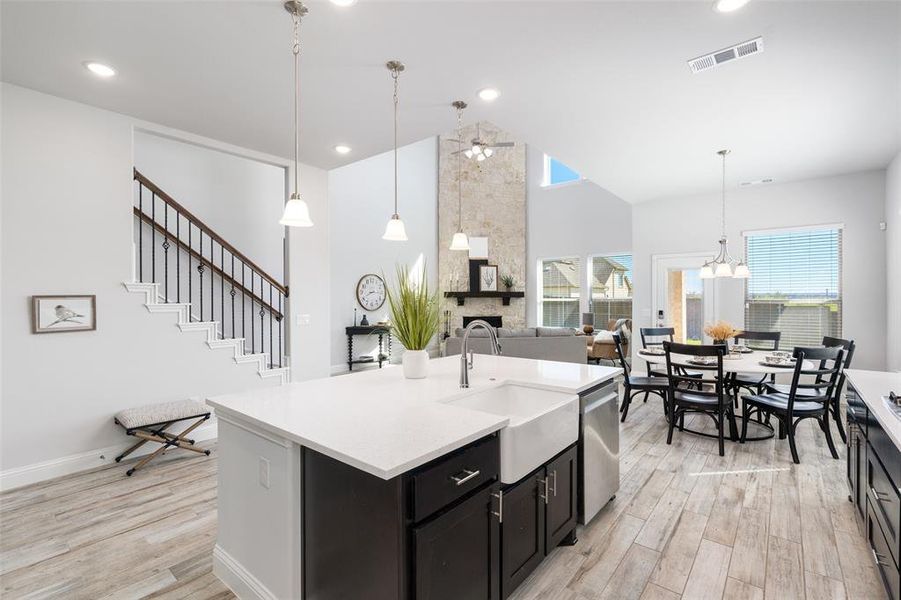 Kitchen featuring light hardwood / wood-style floors, an island with sink, dishwasher, decorative light fixtures, and sink