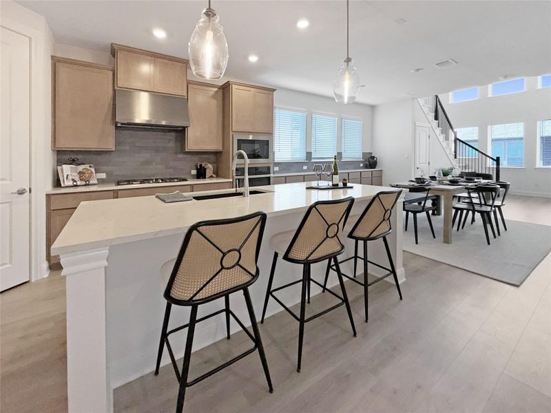 Kitchen with light wood finished floors, a center island with sink, and pendant lighting