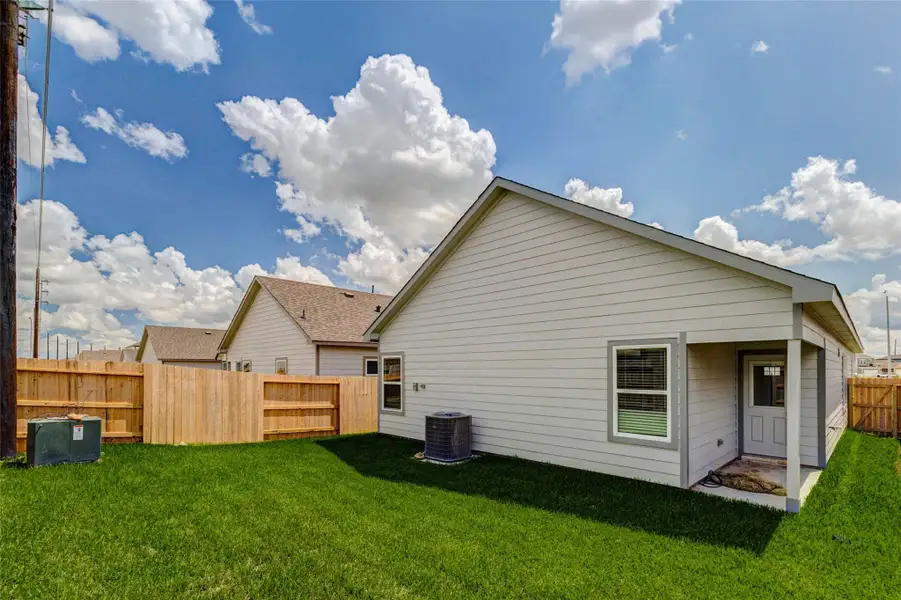Fenced backyard with green lawn, rear exterior view, side yard space, and a covered patio area near the back door. This outdoor space offers room for pets, play, grilling, or relaxing while maintaining an easy-care yard.