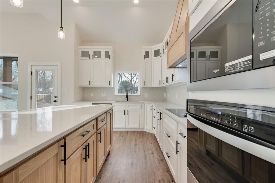 Kitchen featuring stainless steel microwave, oven, pendant lighting, glass insert cabinets, and light brown cabinets