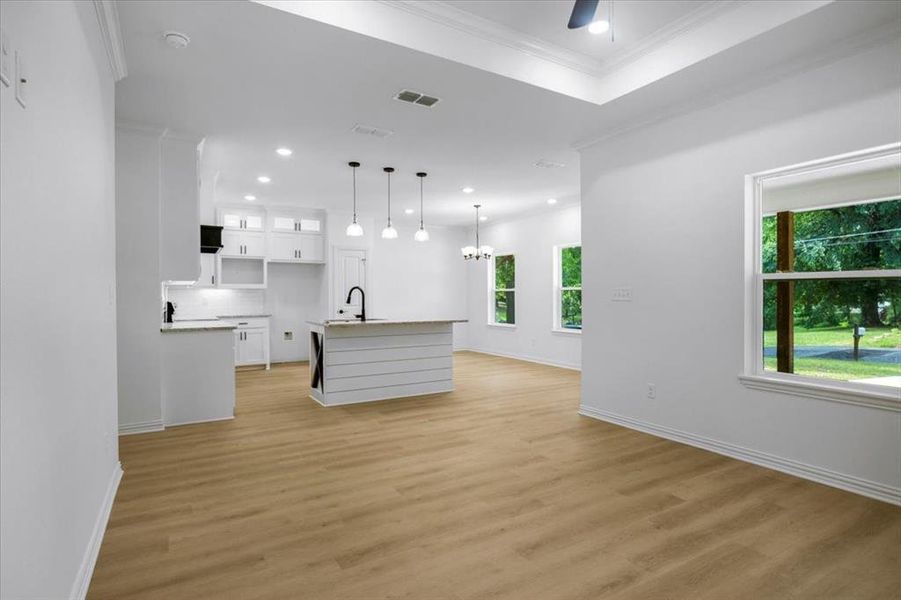 Kitchen featuring white cabinetry, a center island with sink, a chandelier, decorative light fixtures, and ornamental molding