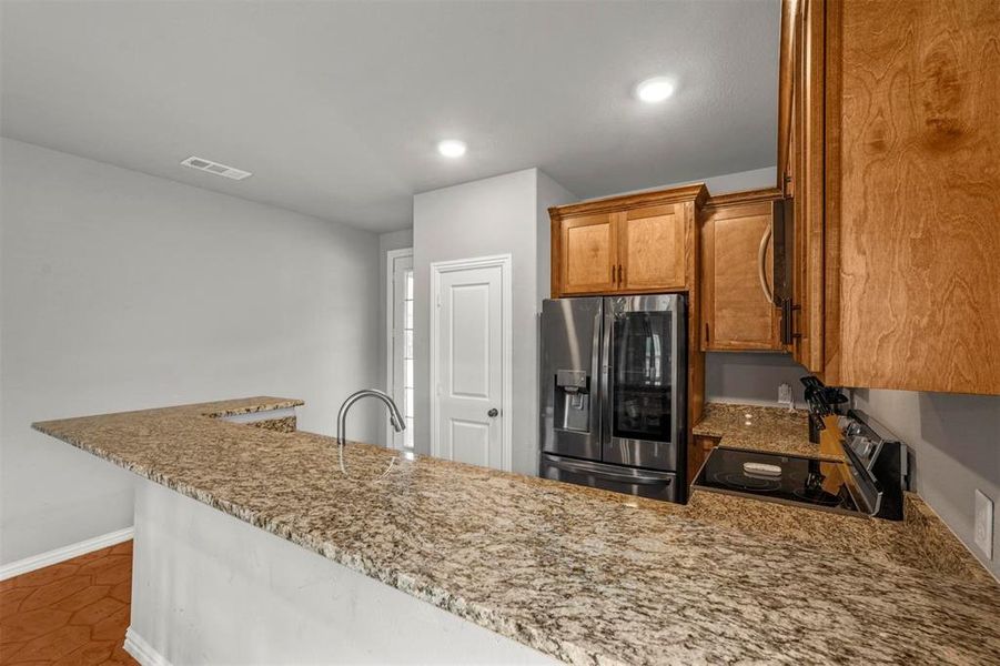 Kitchen with dark patterned flooring, light stone countertops and kitchen peninsula