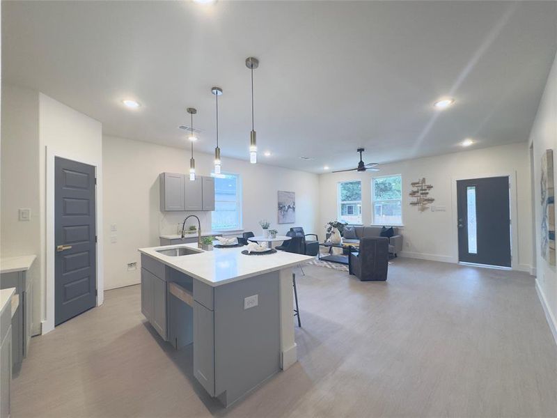 Kitchen with an island with sink, sink, gray cabinets, ceiling fan, and light wood-type flooring