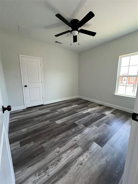 Empty room with visible vents, baseboards, dark wood-type flooring, and a ceiling fan