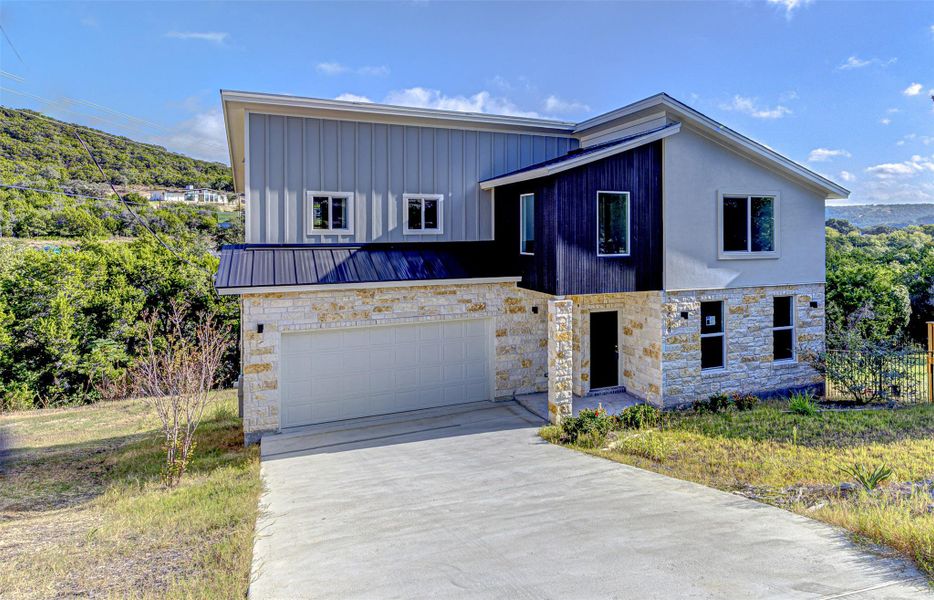 Contemporary house featuring stone siding, concrete driveway, an attached garage, and a metal roof