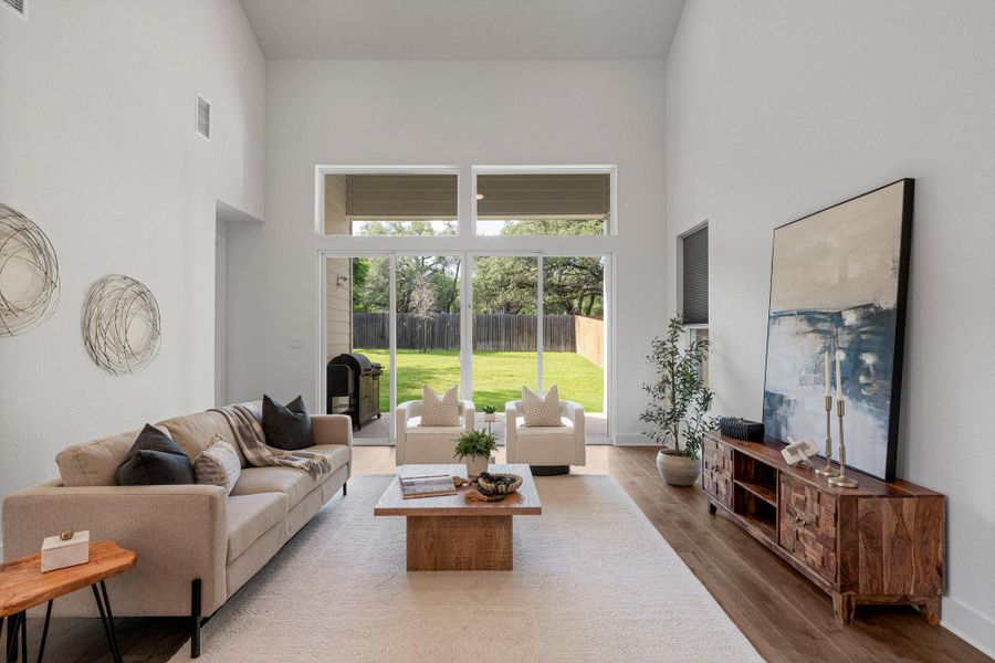 A spacious living room offers high ceilings and abundant natural light through large windows overlooking a green yard.