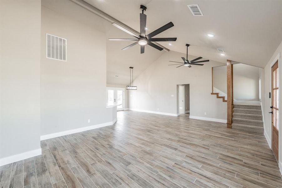 Unfurnished living room featuring stairway, high vaulted ceiling, light wood-style flooring, a ceiling fan, and recessed lighting Unfurnished living room featuring stairway, high vaulted ceiling, light wood-style flooring, a ceiling fan, and recessed lighting