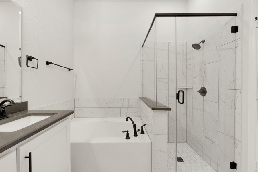 Bathroom with soaking tub, glass walk-in shower, marble tile, and white cabinets with dark hardware