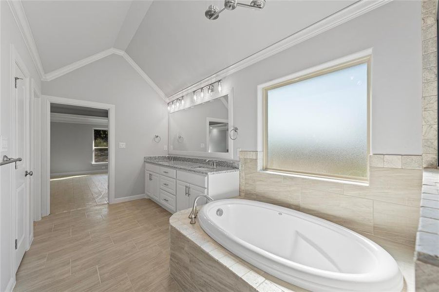 Bathroom with vanity, lofted ceiling, tiled tub, and crown molding