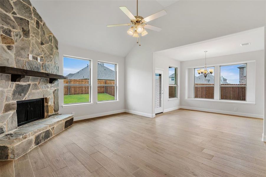 Unfurnished living room with light wood-type flooring, lofted ceiling, a fireplace, a chandelier, and a ceiling fan