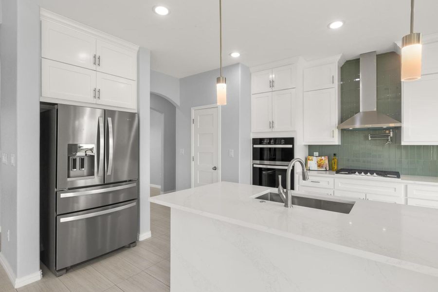 Kitchen with stainless steel fridge with ice dispenser, wall chimney range hood, arched walkways, white cabinetry, and decorative backsplash Kitchen with stainless steel fridge with ice dispenser, wall chimney range hood, arched walkways, white cabinetry, and decorative backsplash