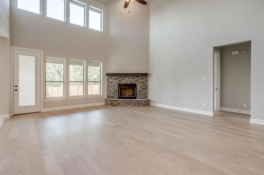 Unfurnished living room featuring ceiling fan, a high ceiling, light wood-type flooring, and a fireplace