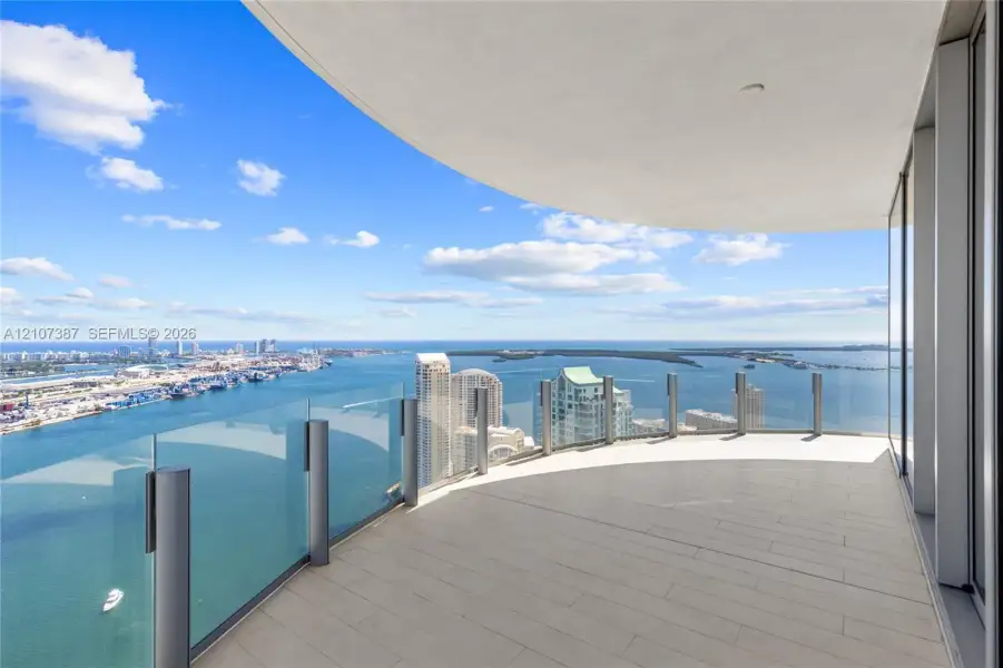 Curved balcony featuring tile flooring, glass panel railings, and panoramic coastal and urban scenery
